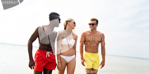 Image of happy friends walking along summer beach