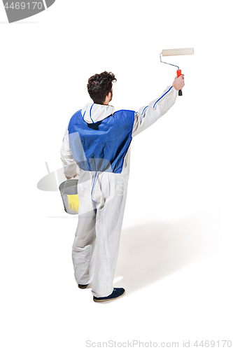 Image of Young male decorator painting with a paint roller climbed a ladder isolated on white background.