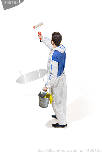 Image of Young male decorator painting with a paint roller climbed a ladder isolated on white background.