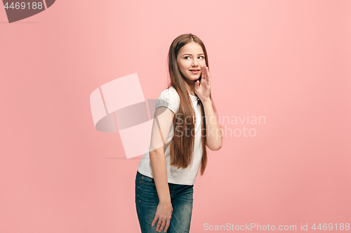 Image of The young teen girl whispering a secret behind her hand over pink background