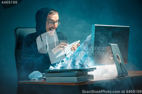 Image of Young stressed handsome businessman working at desk in modern office shouting at laptop screen and being angry about spam