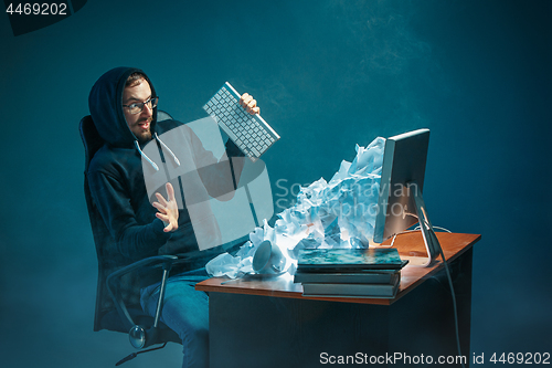 Image of Young stressed handsome businessman working at desk in modern office shouting at laptop screen and being angry about spam