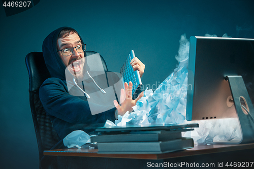 Image of Young stressed handsome businessman working at desk in modern office shouting at laptop screen and being angry about spam