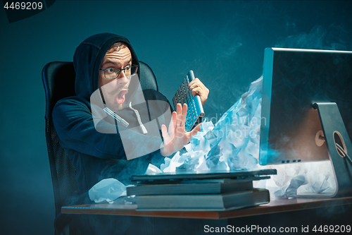 Image of Young stressed handsome businessman working at desk in modern office shouting at laptop screen and being angry about spam