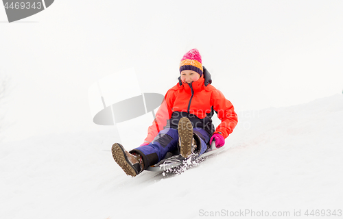 Image of girl sliding down on snow saucer sled in winter