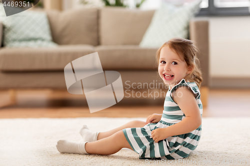 Image of happy baby girl sitting on floor at home