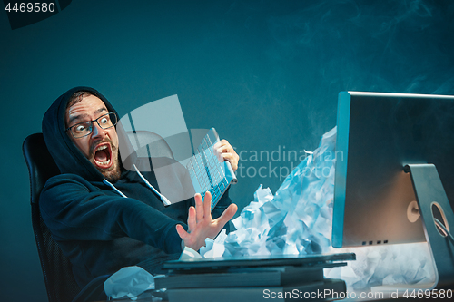 Image of Young stressed handsome businessman working at desk in modern office shouting at laptop screen and being angry about spam