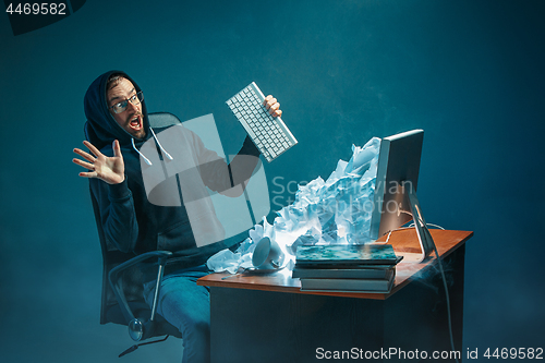 Image of Young stressed handsome businessman working at desk in modern office shouting at laptop screen and being angry about spam