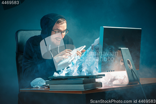 Image of Young stressed handsome businessman working at desk in modern office shouting at laptop screen and being angry about spam