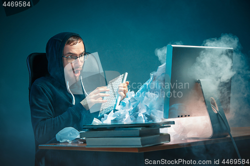 Image of Young stressed handsome businessman working at desk in modern office shouting at laptop screen and being angry about spam