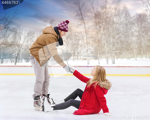 Image of man helping woman to get up from skating rink