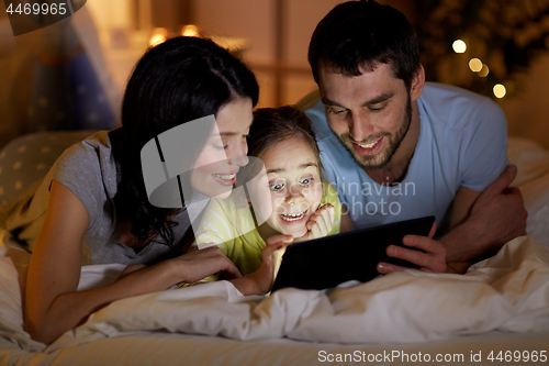 Image of family with tablet pc in bed at night at home