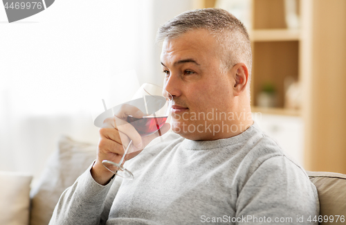 Image of man drinking red wine from glass at home