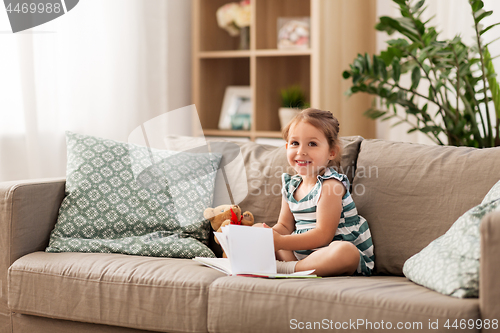 Image of happy girl sitting on sofa with book at home