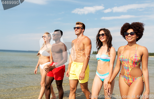 Image of happy friends walking along summer beach