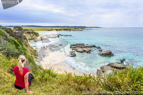 Image of Female sitting by the coastal bluff looking out to the rocky beach belo