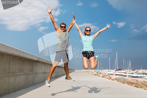 Image of happy couple in sports clothes jumping on pier