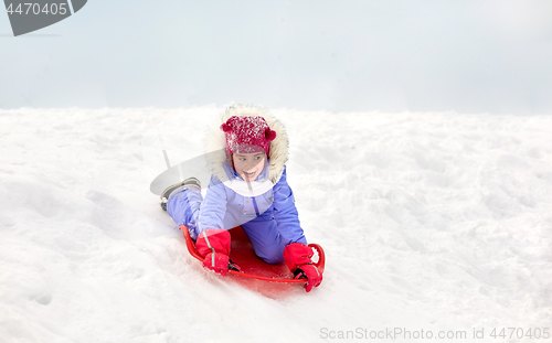 Image of girl sliding down on snow saucer sled in winter