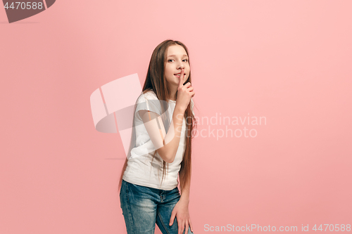 Image of The young teen girl whispering a secret behind her hand over pink background