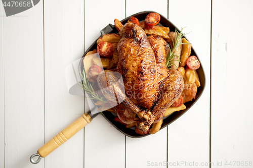 Image of Grilled whole chicken in cast iron black pan with potatoes, tomatos and rosemary