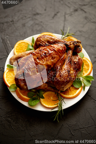 Image of Roasted whole chicken or turkey served in white ceramic plate with oranges