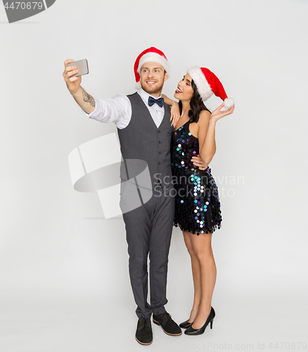 Image of couple in santa hats aking selfie at christmas