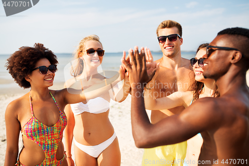 Image of happy friends making high five on summer beach