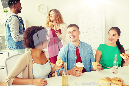 Image of happy friends or team eating at office