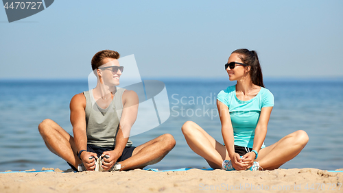 Image of smiling couple stretching legs on beach