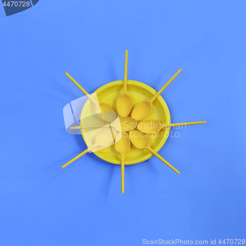 Image of A yellow plastic plate and spoons lay around it on a bright blue background. The concept of a holiday, picnic.