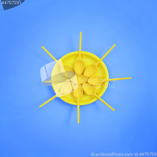 Image of A yellow plastic plate and spoons lay around it on a bright blue background. The concept of a holiday, picnic.