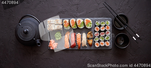 Image of Assortment of different kinds of sushi rolls placed on black stone board