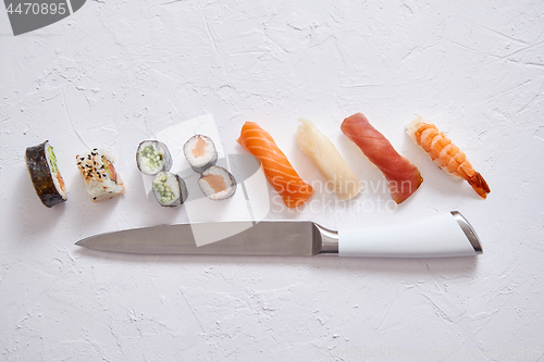 Image of Various sushi rolls with Japanese knife on white stone slate background