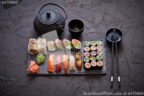 Image of Assortment of different kinds of sushi rolls placed on black stone board