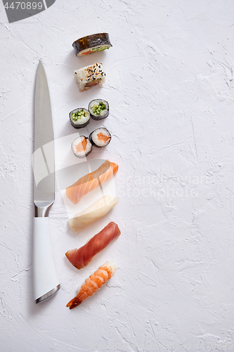 Image of Various sushi rolls with Japanese knife on white stone slate background