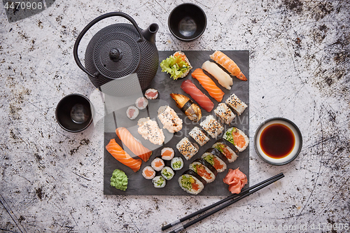 Image of Assortment of different kinds of sushi rolls placed on black stone board