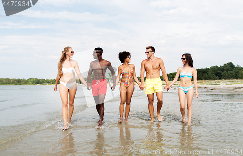 Image of happy friends walking along summer beach