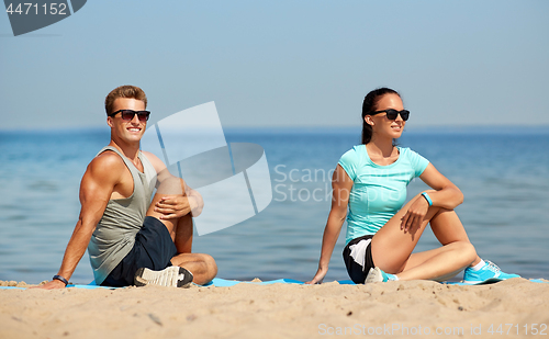 Image of smiling couple stretching legs on beach