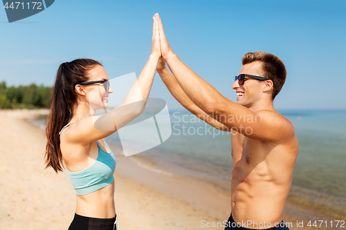 Image of happy couple in sports clothes and shades on beach