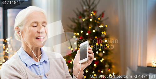 Image of senior woman with smartphone and earphones at home