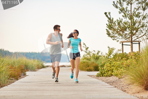 Image of couple in sports clothes running along beach path