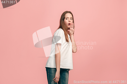 Image of The young teen girl whispering a secret behind her hand over pink background