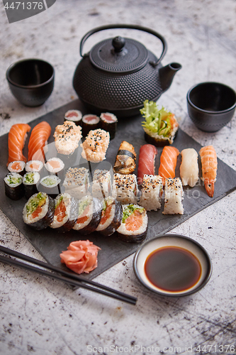 Image of Assortment of different kinds of sushi rolls placed on black stone board