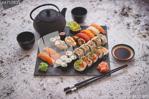Image of Assortment of different kinds of sushi rolls placed on black stone board