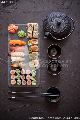 Image of Assortment of different kinds of sushi rolls placed on black stone board