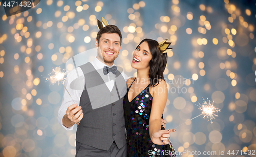 Image of happy couple with crowns and sparklers at party