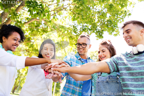 Image of happy smiling friends stacking hands in park