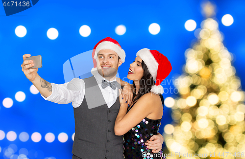 Image of couple in santa hats aking selfie on christmas