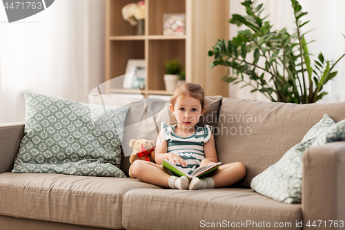 Image of happy girl sitting on sofa with book at home