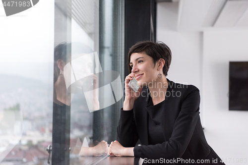 Image of Elegant Woman Using Mobile Phone by window in office building